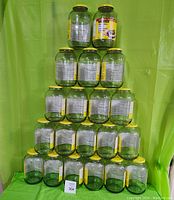 Full view of 20 clean empty glass pickle jars stacked in a pyramid, each with yellow lids and labels.