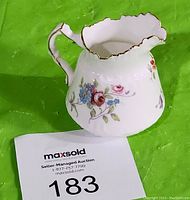 Side view showing the floral design and gold rim on the creamer along with MaxSold lot number card.