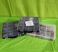 Three closed plastic partitioned cases shown on green cloth background.