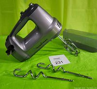Silver and black Moulinex hand mixer model 216716 with attached beaters, two dough hooks and a storage case placed on a green background.