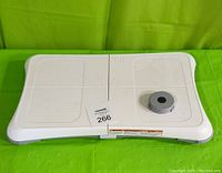 Front view of white Nintendo Wii Balance Board with textured foot pads, extra grey foot accessory on top, displayed on green background