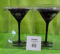 Pair of black martini glasses in clear plastic packaging showing full glasses and skull design