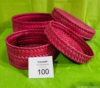 Pair of two red round woven nesting boxes with lids shown closed side by side on green background. Box sizes clearly visible and weave texture.