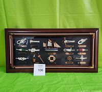 Front view of the wooden shadow box with multiple maritime miniature items under glass, displayed against a green backdrop with lot number card 106.