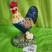 Front and side view of the Partylite ceramic tea light candle holder shaped as a rooster with chicks standing on a grassy base.