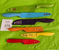 Six kitchen knives laid out with colored protective covers matching handles on green background