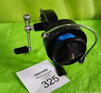 Side angle view of the Garcia Mitchell 300 fishing reel showing handle and line spool with blue fishing line on a green background with auction tag.