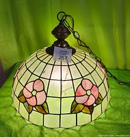 Front angle showing pink flower designs on cream colored stained glass with metal hanging hardware and chain