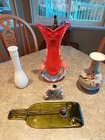 Front and side angle of the art glass red goldfish vase, the white milk glass vase, the oriental floral vase, drilled stone candleholder, and green glass dish with candle snuffer.
