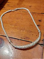 Full view of the vintage 925 sterling silver necklace laid out flat on wooden surface, displaying the woven chain and curved engraved centerpiece.