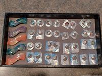 Top view of the complete set of 21 multicolored hair clips and multiple pairs of mother of pearl earrings arranged in a tray.