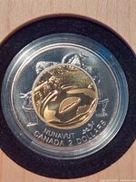 Close-up of the $2 coin showing the 'Founding of Nunavut' design by Germaine Arnaktauyok in a protective capsule inside the box.