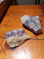 Two amethyst and quartz geode gemstone samples placed on wooden surface showing rough crystalline textures and natural coloration.