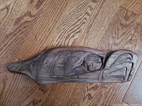 Top-down photo of wooden eagle carving on wooden floor, showing detailed stylized bird design and natural wood texture.
