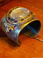 Close-up of the front and top side showing the molten glass stone in the ornate brass setting with decorative details and patina.