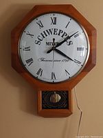Front view of vintage wooden octagonal wall clock with Schweppes branding and Roman numerals on white face, showing the entire clock including pendulum case and power cord.