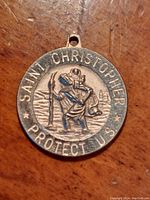 Close-up front view of round sterling silver medallion depicting Saint Christopher carrying the Christ child, inscribed around the edge 'Saint Christopher Protect Us'.