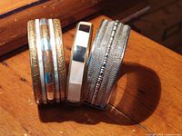 Three vintage metal and mother of pearl bracelets stacked together on wood surface showing texture and color details.
