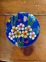 Top view of the cloisonne lidded container showing detailed floral and butterfly enamel design on blue background.