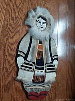 Close-up front view of vintage Yupik reindeer fur and leather figure art displayed on wooden floor.