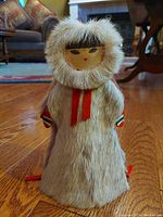Front view of the Indigenous Siberian Yupik doll showing fur hood, painted wooden face with simple features, and red fabric ties on cloak.