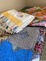 View of three folded quilts stacked, showing various patchwork and colors