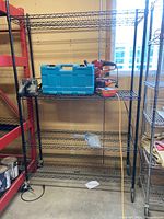 Full view of the black metal shelving unit with a blue toolbox and red power tools on the top shelf. Shown in a garage environment.
