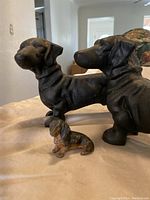 Three dachshund figurines shown grouped together: two large black cast iron doorstops and one small black and tan miniature dachshund.