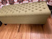 Side view of the tufted top and cloth texture of the storage bench, showing chartreuse fabric and wooden legs.