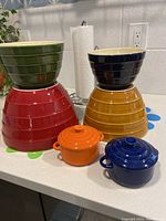Set of 4 colorful mixing bowls stacked with 2 small covered sauce bowls in front, colors include green, navy, red, yellow, orange, and blue.