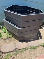 Side view showing two stacked hexagonal shaped plastic raised garden beds with wood-grain texture, placed outdoors next to a house wall on a stone pathway.
