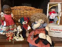 Wide shot showing two Campbell kids dolls, multicolored plush bear, white horse figurine, small figurine, large woven basket and boxed "Little Cowboy" doll