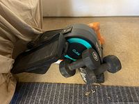 Angle view of Cubii elliptical and some dumbbells on carpet showing black unit with teal accent and black and orange dumbbells.