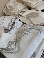 Close-up photo of assorted napkins, placemats, and doilies in natural and neutral tones showing embroidered and scalloped details.