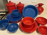 Full set view showing all items including large red canisters with lids, red pitcher, lapis blue and red bowls, plates, and mugs arranged on countertop