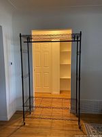 Front view of the black metal garment rack showing three wire shelves and the removable hanging bar.