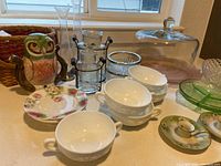 Wide view of the collection showing ceramic owl pitcher, tea cups and saucers, cake plate, various glass vases and holders.