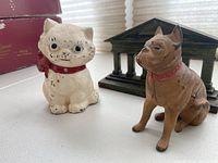 Front view of the cast iron kitten bank, boxer dog bank, and Parthenon bookend showing wear and paint chipping on banks and detailed architectural design of bookend.