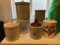 Image showing six vintage stoneware crocks of various sizes and designs set on a table with natural light from window behind
