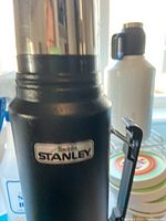Close-up photo of the Stanley insulated thermos with textured green body and stainless steel top showing the Stanley brand label.