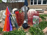 Overview of garden items including red metal tomato cages, garden netting, umbrella fan, sprayer, and garden tools
