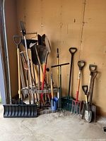 Front view of various garden tools including shovels, pitchforks, rakes, stored in plastic rack in garage
