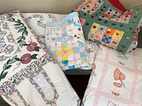 Full view of five quilts folded together showing variety of patchwork, floral and appliqué patterns in different colors and sizes, emphasizing the lot contents