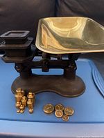 Full view of antique balance scale with brass pan and various black rectangular and cylindrical brass weights.