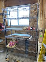 Full front view of the six-tier silver metal wire shelving unit with items on some shelves (not included in sale). The shelving stands in a garage by a window, showing its scale and general condition.