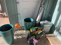 Photo showing two tall teal plastic planters, a metal trash can with lid, metal rack, modular vertical garden planter packaging, and boxed garden edging.