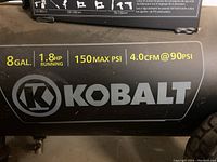 Close-up of tank label showing 8 gallon, 1.8 horsepower, maximum 150 PSI, and 4.0 CFM at 90 PSI specifications with Kobalt logo.