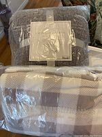 Two wearable blankets in original packaging, one gray chenille sherpa and one neutral plaid