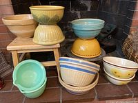 Full view of group of 11 vintage bowls of assorted colors, textures and sizes arranged on and near a small wooden stool.