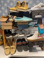 Overall lot showing variety of shoes on a metal rack, including yellow hiking boots, blue espadrilles, colorful clogs, tan loafers, and sneakers.